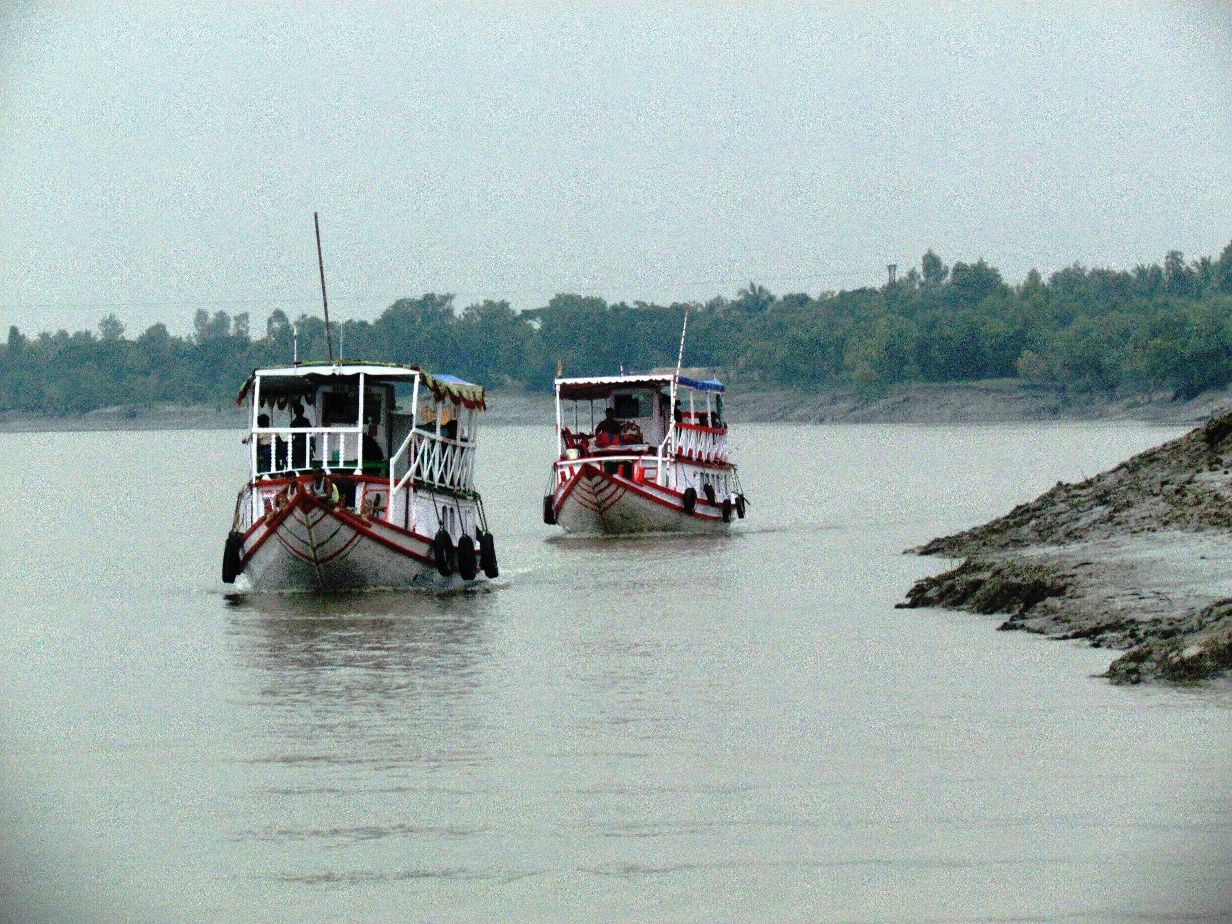 Two boats on a calm river with a forested shoreline.