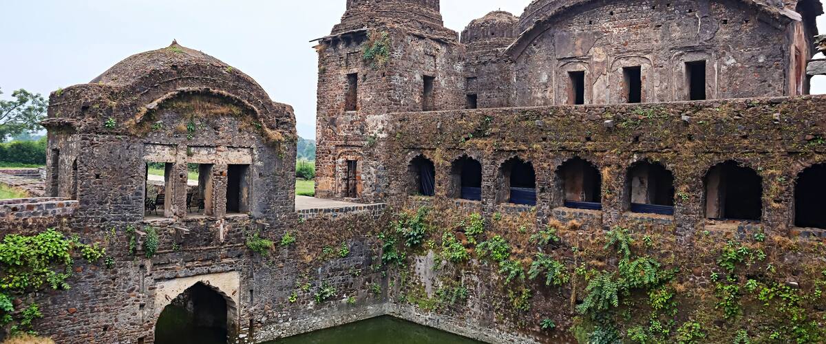 An ancient stone structure with domed roofs and arched windows, partially overgrown with vegetation.