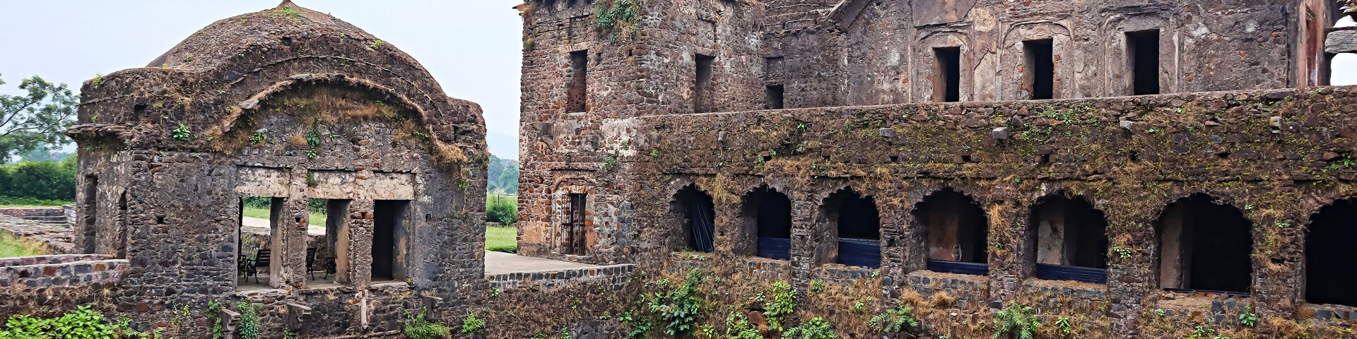 An ancient stone structure with domed roofs and arched windows, partially overgrown with vegetation.
