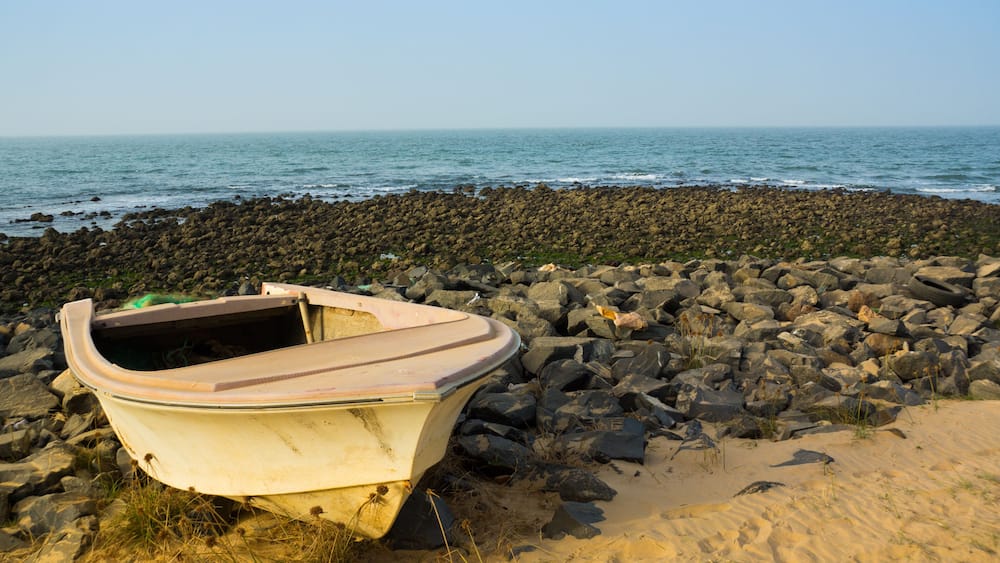 A small boat on a rocky beach with the ocean in the background.