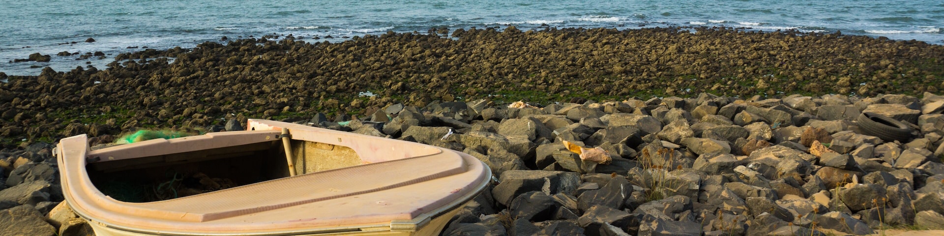 Ein kleines Boot an einem felsigen Strand, im Hintergrund das Meer.