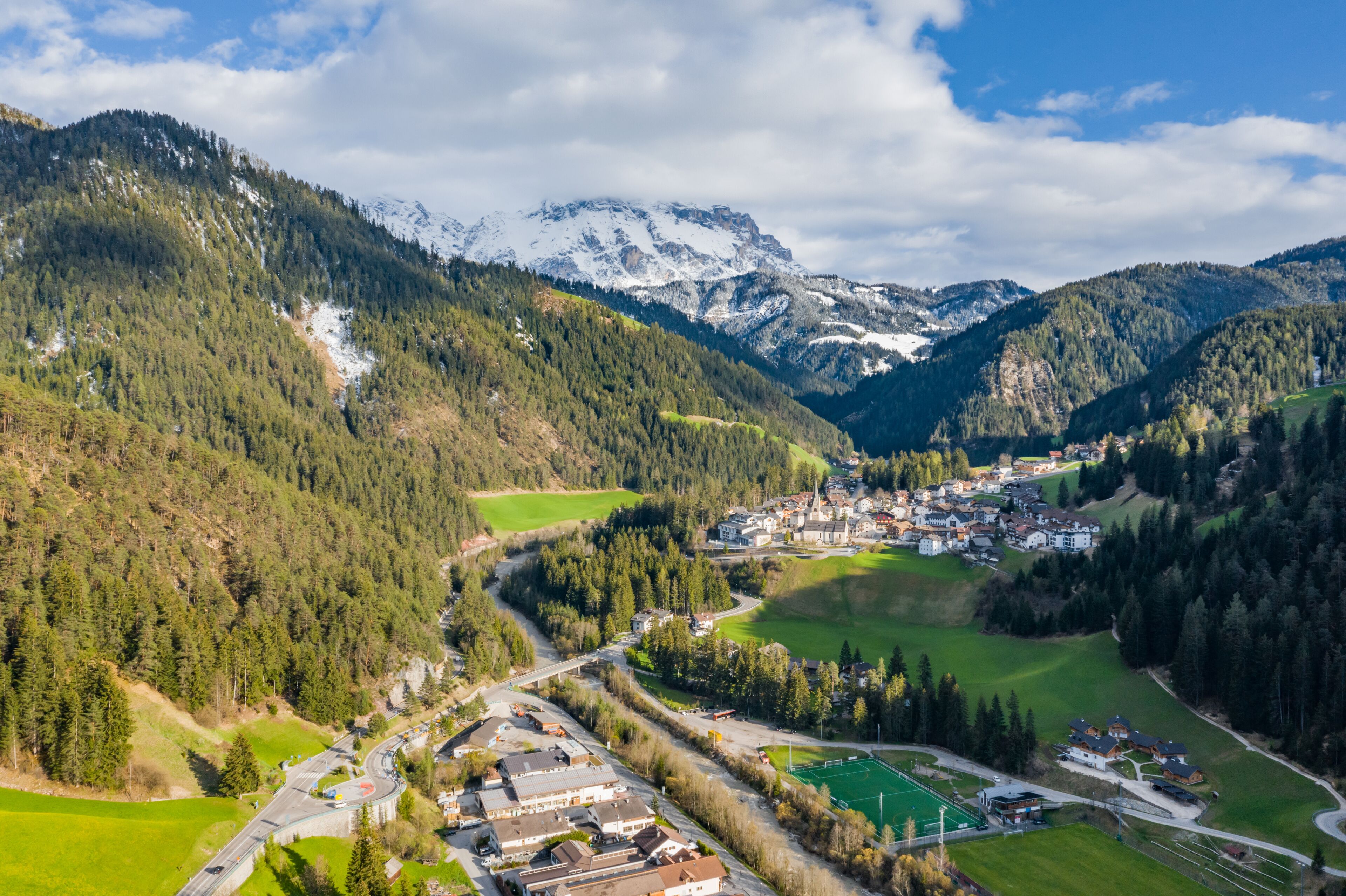 A mountainous landscape with a village nestled in a valley, surrounded by dense forests and snow-capped peaks.