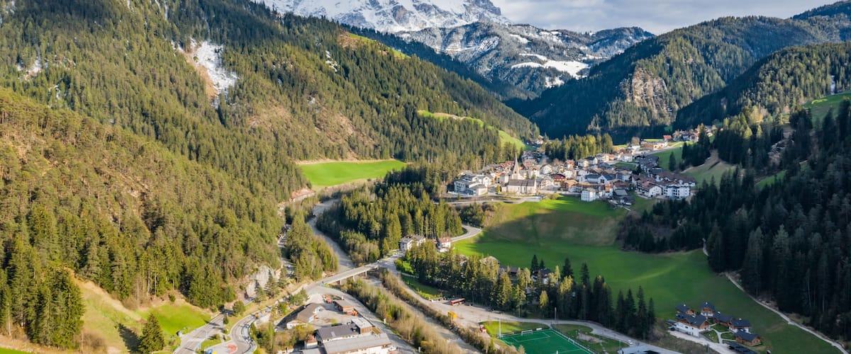 A mountainous landscape with a village nestled in a valley, surrounded by dense forests and snow-capped peaks.