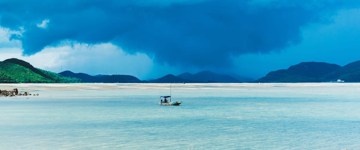 A calm sea with a small boat in the foreground and a stormy sky above.