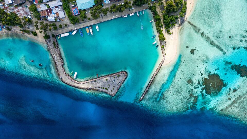 Aerial view of local, inhabited island Felidhoo, located in Vaavu Atoll, Maldives, Indian Ocean with boats / dhonis anchored in the harbour and local beach