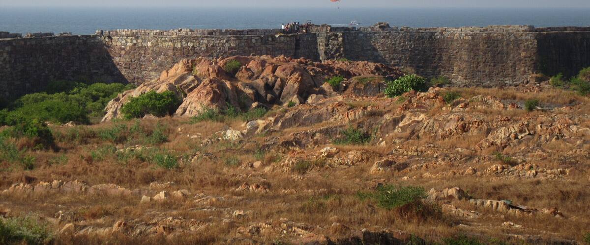 A coastal fortification with a view of the sea and a hot air balloon in the distance.