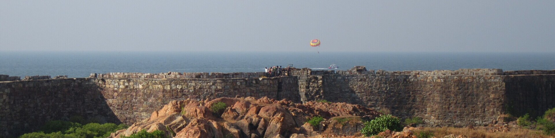 A coastal fortification with a view of the sea and a hot air balloon in the distance.