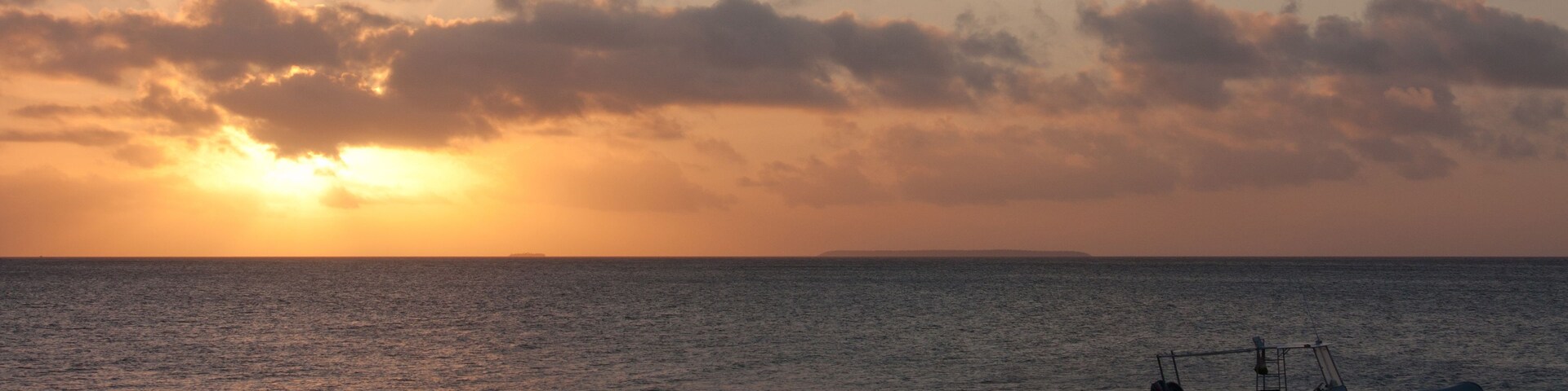 Um barco em águas calmas durante o pôr do sol, com céu nublado.