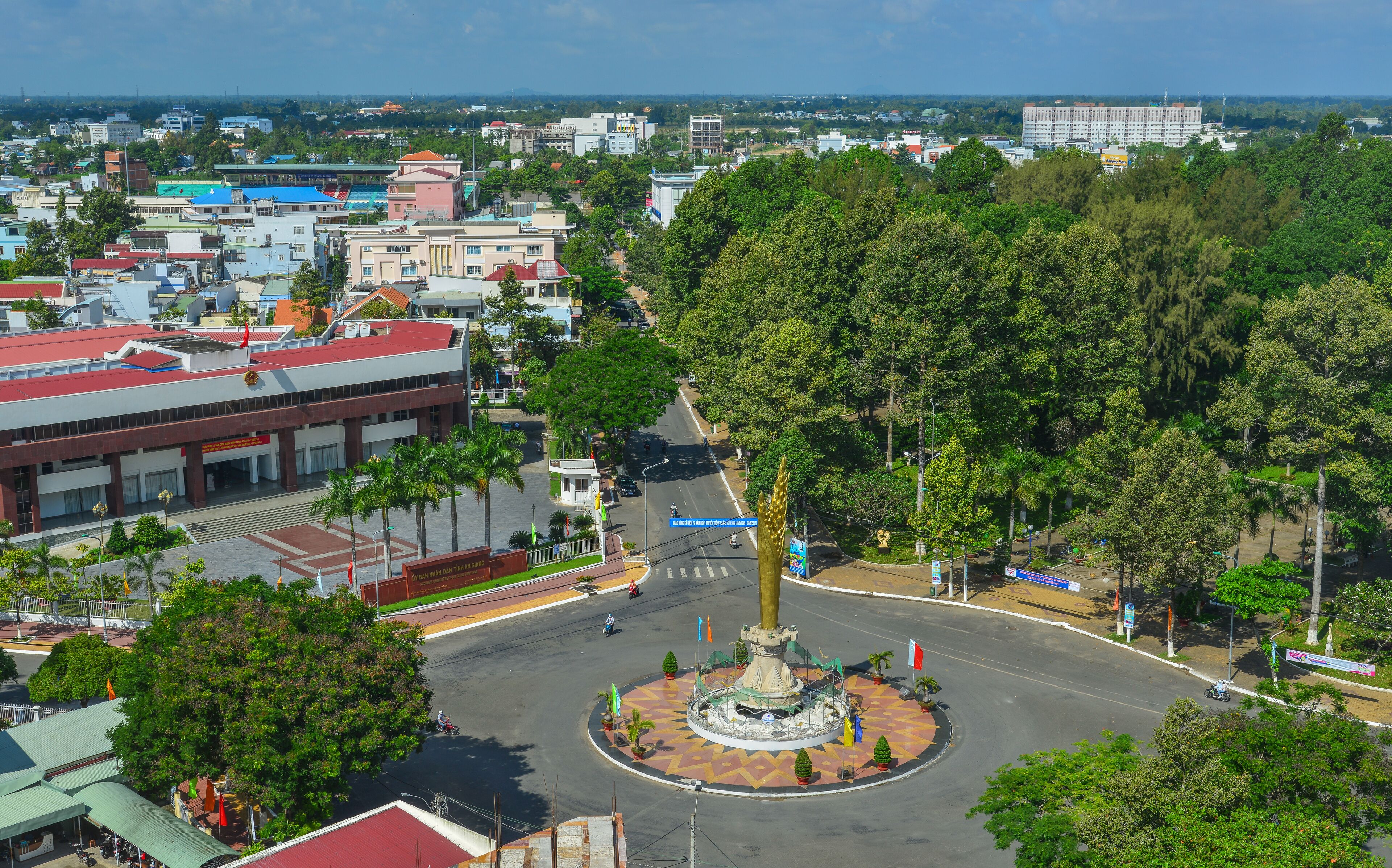 A cityscape with a central roundabout, surrounded by buildings and lush greenery.