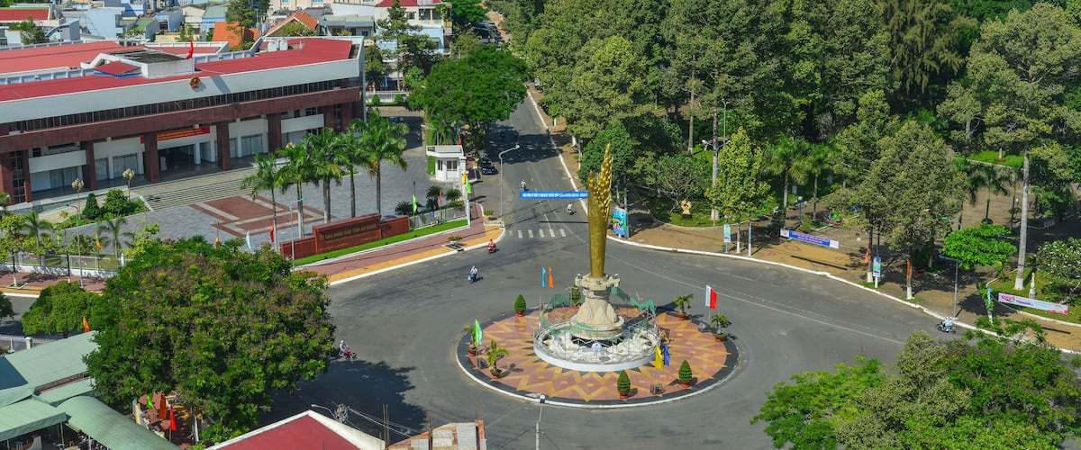 A cityscape with a central roundabout, surrounded by buildings and lush greenery.