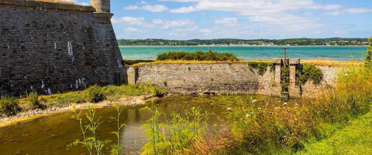A stone fortification with a watchtower overlooking a river and a distant shoreline.