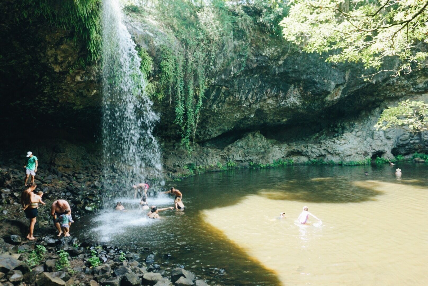 A waterfall in a cave with people enjoying the water.