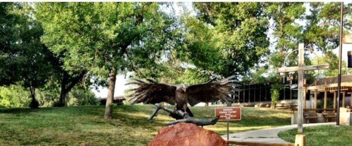 A large rock with a bird sculpture and a sign in a park.