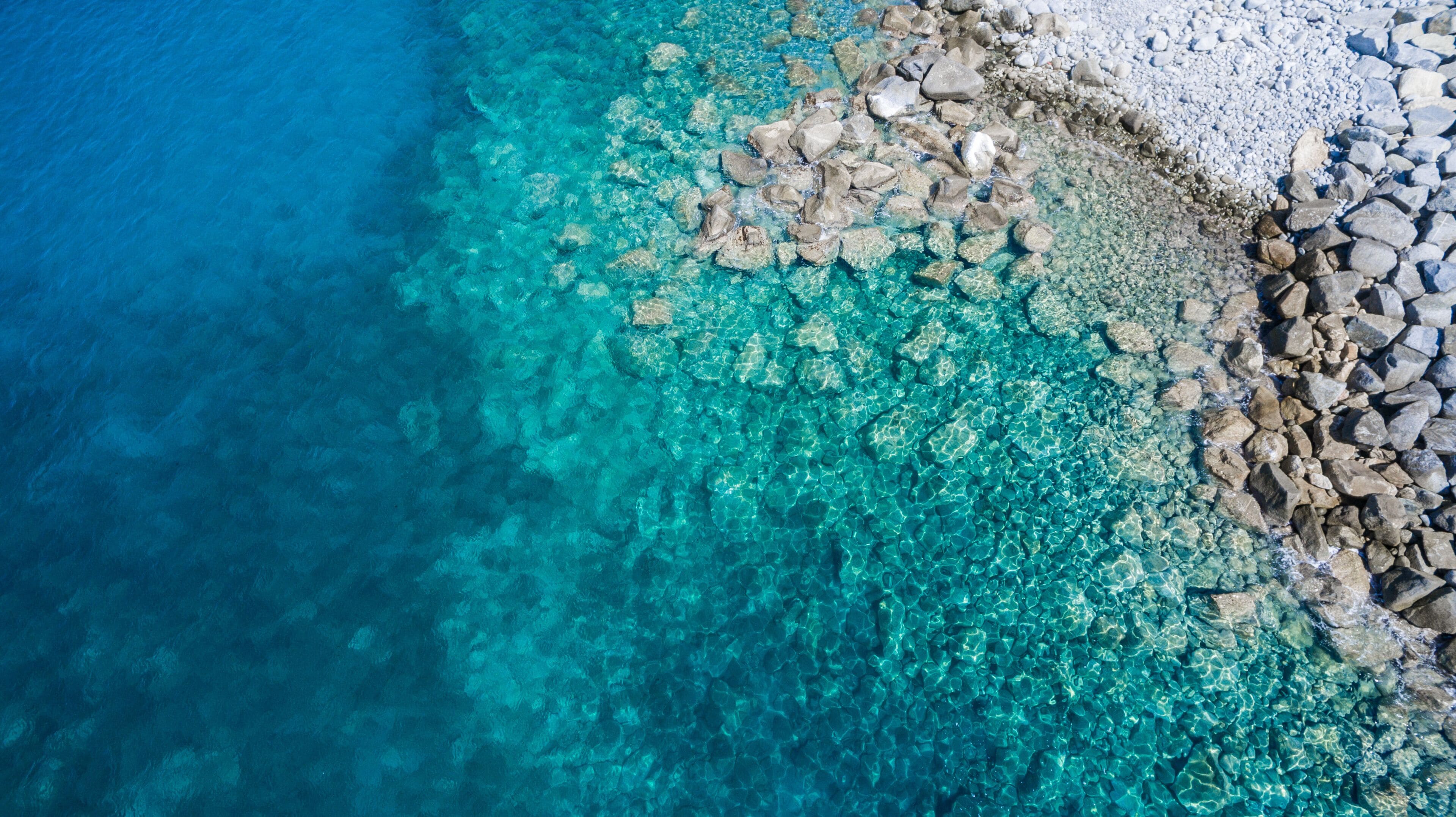 Un mar turquesa transparente con rocas visibles bajo el agua y una costa rocosa.