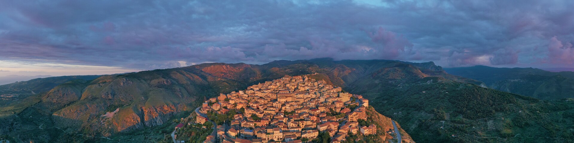 A mountainous town nestled in a valley with winding roads and dense greenery.