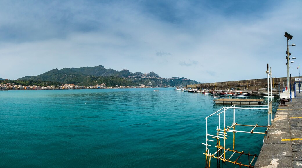 A coastal cityscape with a clear view of the sea, a prominent mountain in the background, and a harbor with boats.