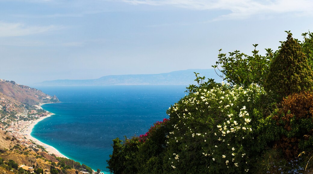 A coastal landscape with a winding road, a beach, and a mountainous backdrop.