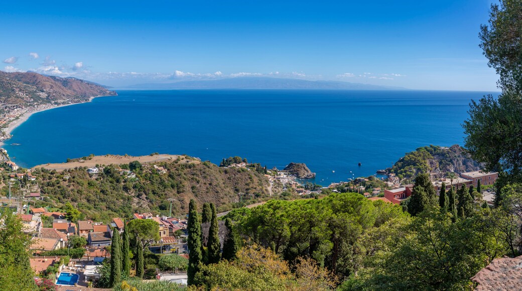 A coastal town with a clear view of the sea, surrounded by hills and dense greenery.