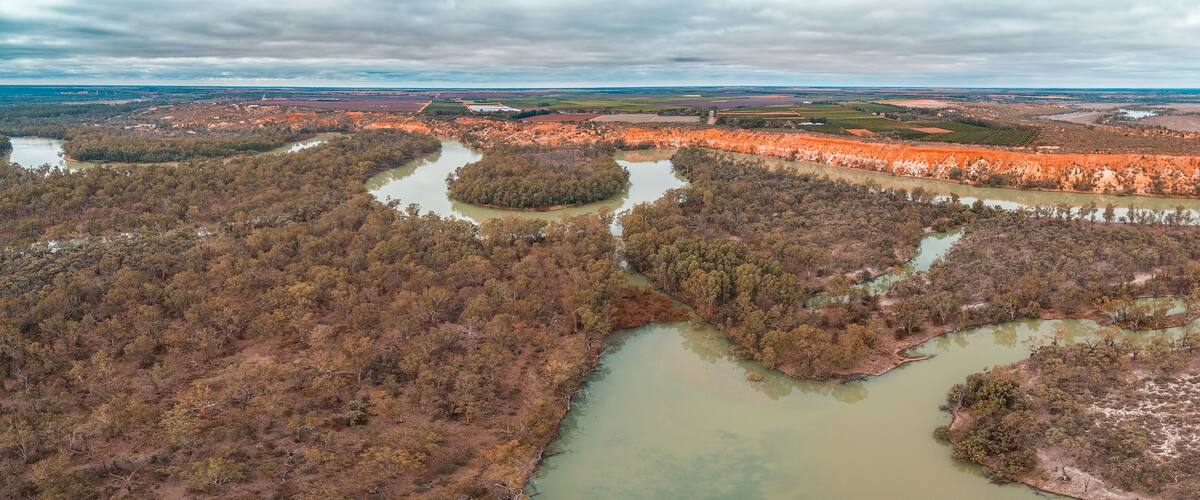 An aerial view of a river winding through a forested area with patches of red soil.
