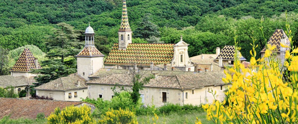 A village with traditional architecture, including a church with a tall spire and a bell tower, surrounded by lush greenery and yellow flowering plants.
