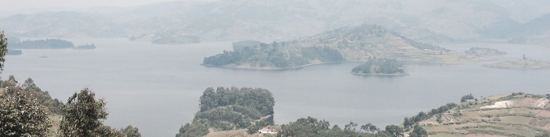 A panoramic view of a lake surrounded by hills and scattered trees.
