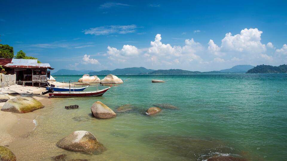 A coastal scene with clear turquoise water, large rocks, and a traditional boat docked near a small wooden structure.