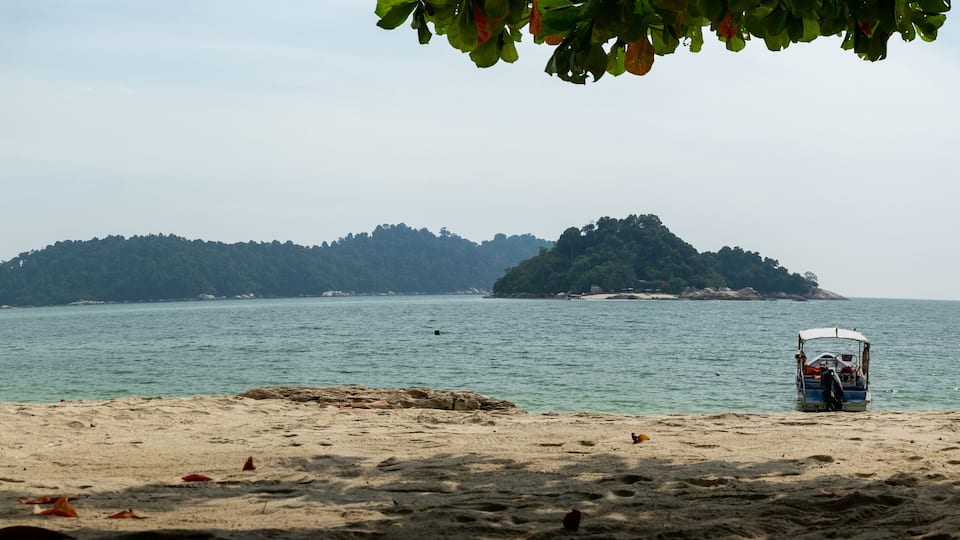 A beach with a boat and a forested island in the background.