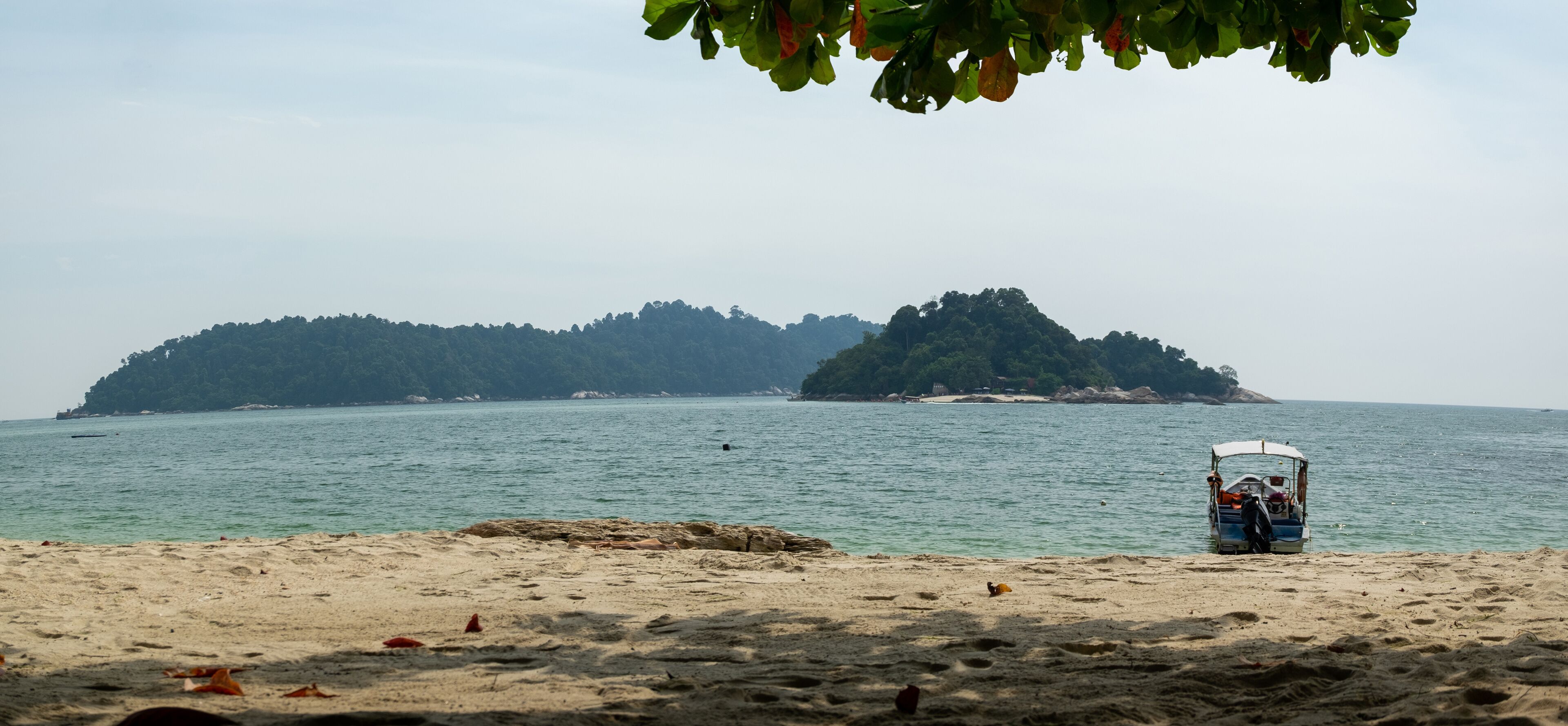 A beach with a boat and a forested island in the background.