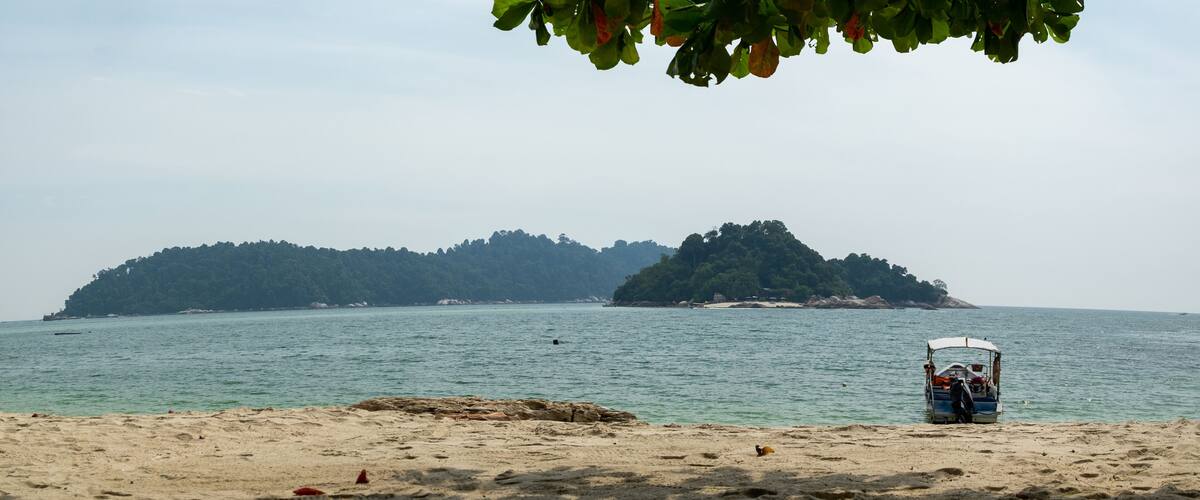 A beach with a boat and a forested island in the background.