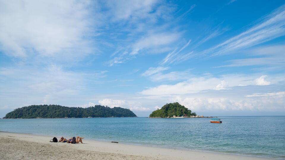 A beach with two small islands in the distance, calm sea, and clear sky.
