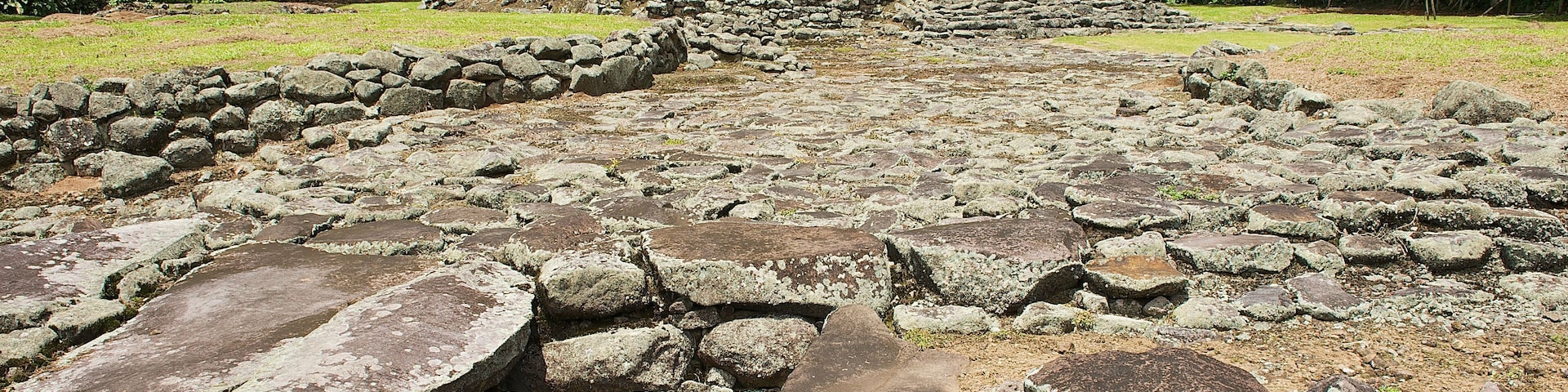 Un sendero de piedra antigua que conduce a un montículo rodeado de árboles.
