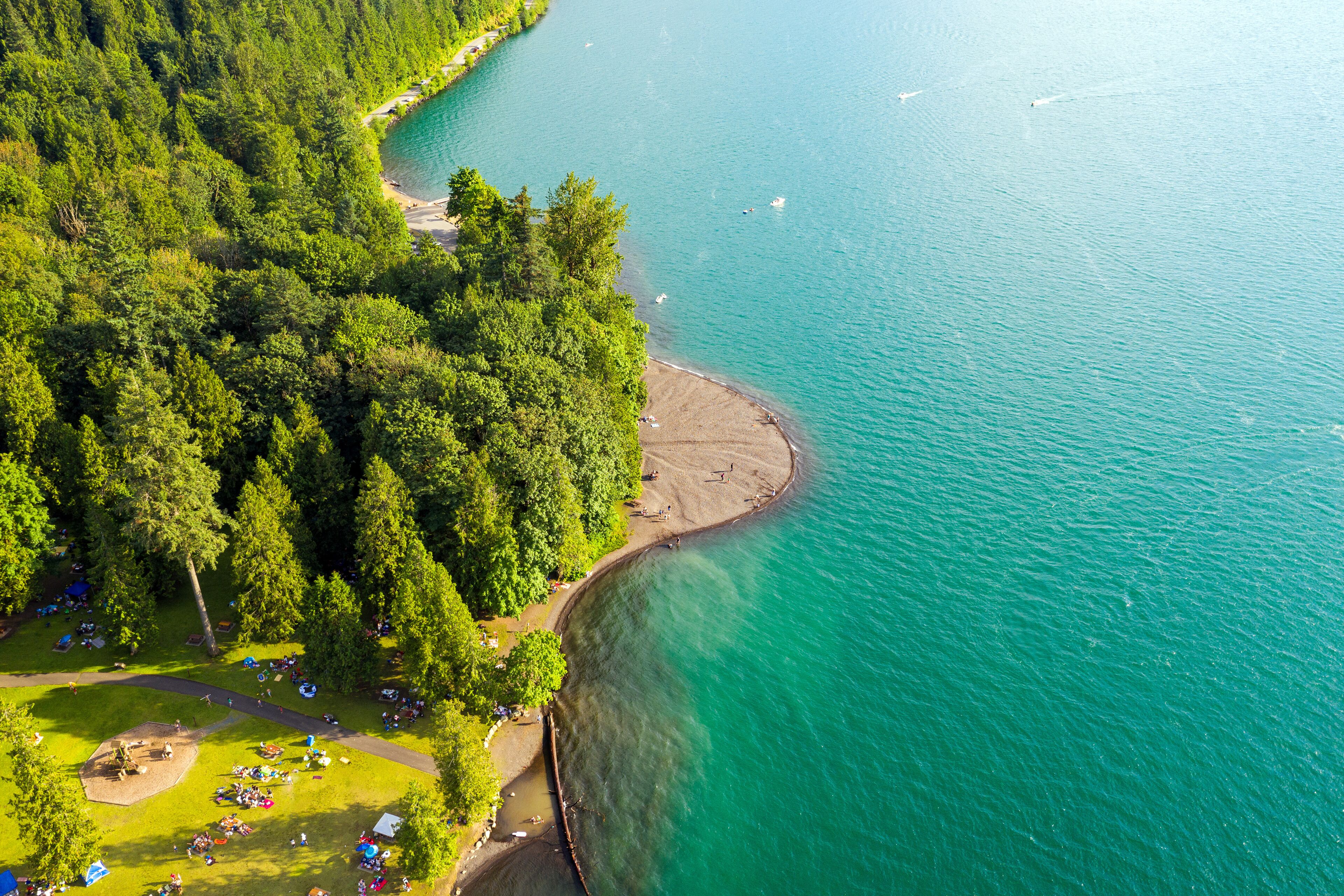 Aerial photo of Cultus Lake in Chilliwack, B.C. while people are enjoying the summer activities at the lakeshore and doing barbeque in the woods by the lake