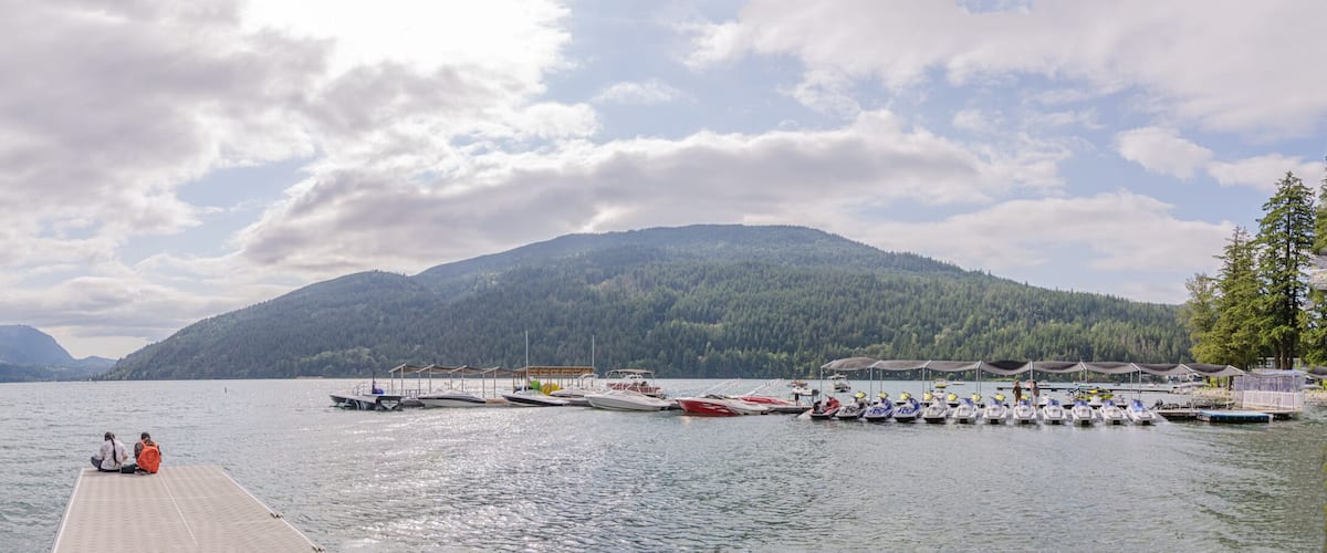 A lake with boats, a dock, and forested mountains in the background.