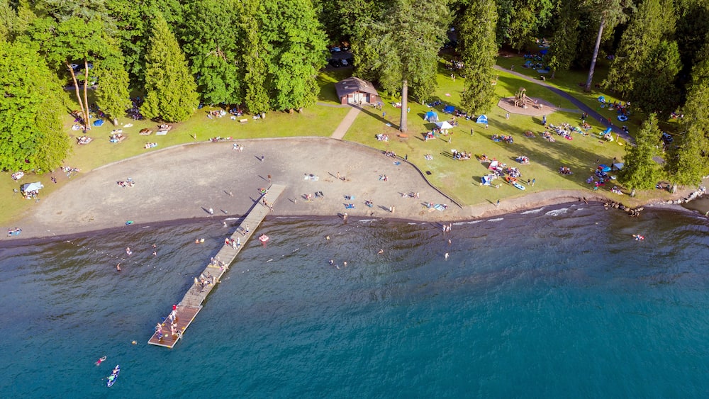 Birds eye view photo of Cultus Lake and its beach while people are enjoying the summer activities at the lakeshore and doing barbeque in the woods by the lake, Chilliwack, British Columbia, Canada