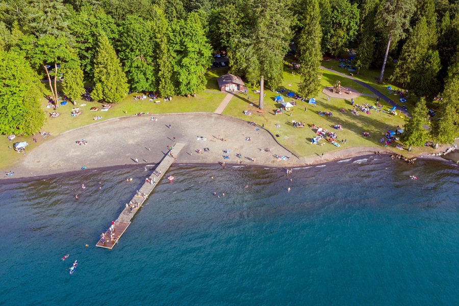 Birds eye view photo of Cultus Lake and its beach while people are enjoying the summer activities at the lakeshore and doing barbeque in the woods by the lake, Chilliwack, British Columbia, Canada