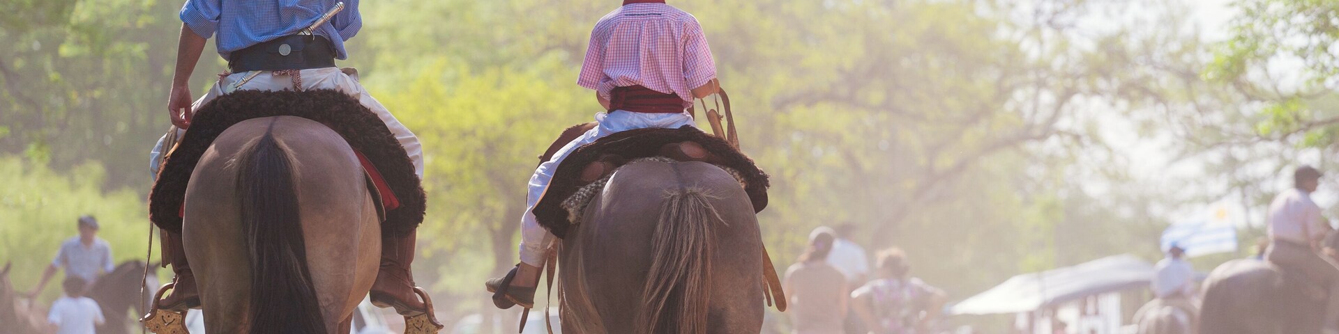 Two people riding horses on a dirt path with trees in the background.