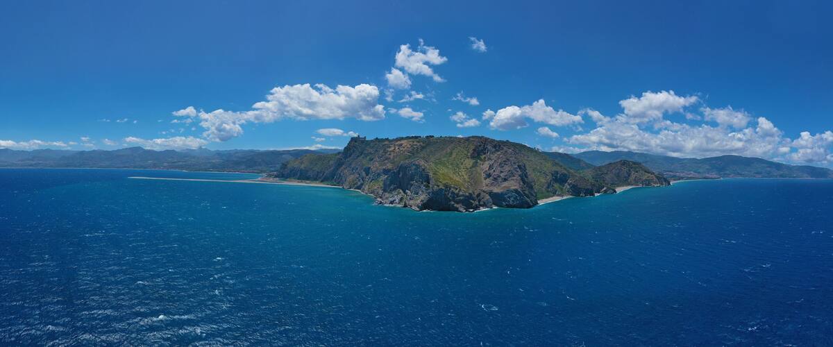 A coastal island with a prominent mountain peak and a clear blue sea.