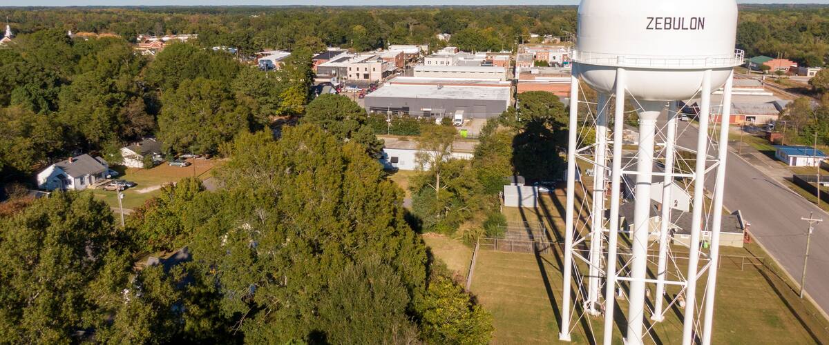 A water tower labeled 'ZEBULON' amidst a town with buildings and trees.