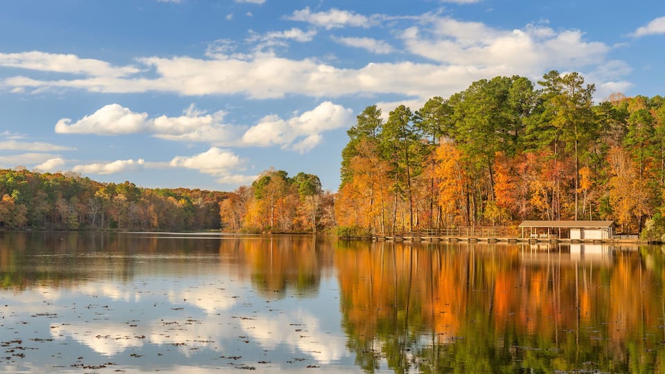 A calm lake surrounded by autumn-colored trees and a small dock.