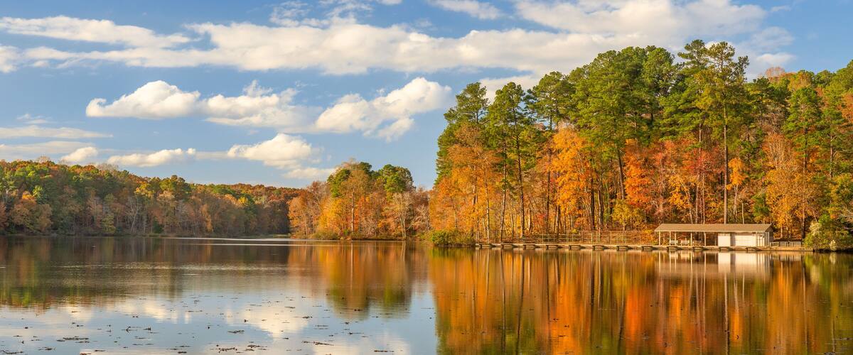 A calm lake surrounded by autumn-colored trees and a small dock.