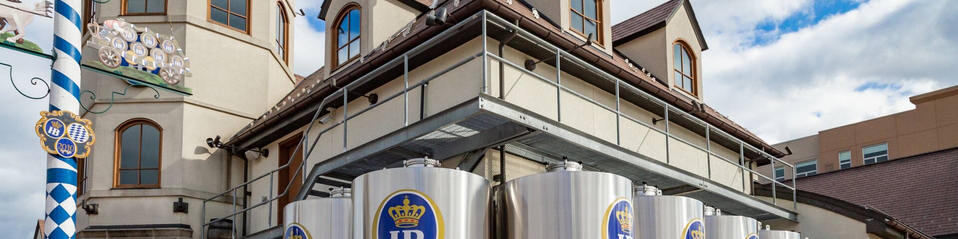 Large stainless steel brewing tanks with logos and text, set against a building with arched windows and a brick facade.