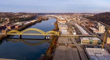 A river with a yellow bridge, a parking lot, and buildings along the riverbank.