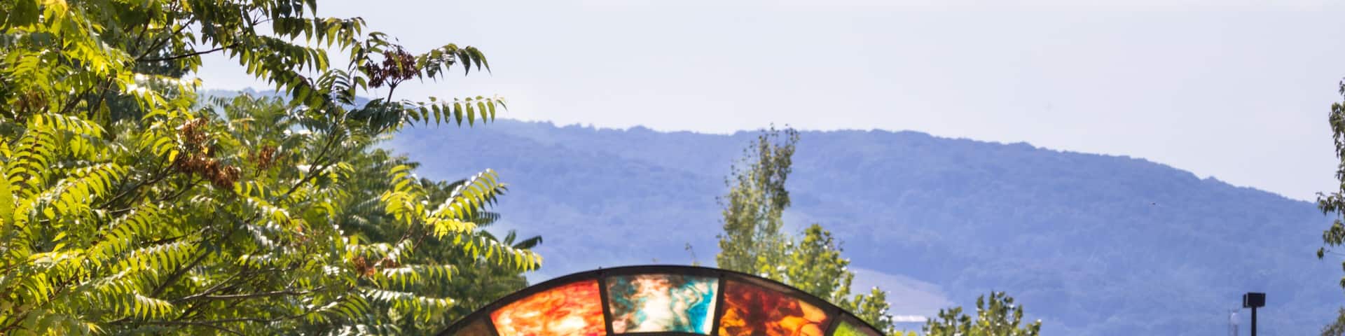 The Great Allegheny Passage rail trail showing colorful opalescent glass arch near Connellsville, PA, with mountain ridge in background