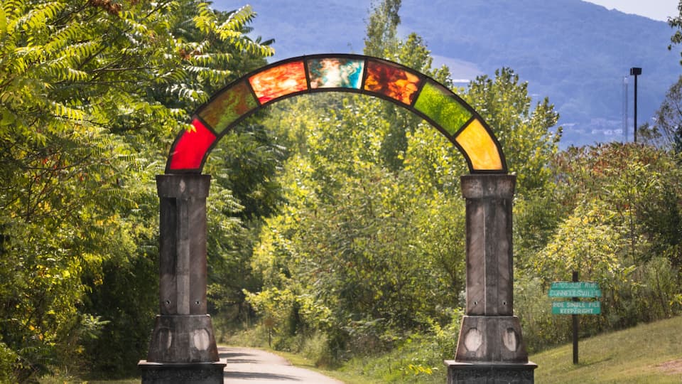 A colorful stained glass archway over a road with a sign reading "Prospect Road Connell's Swell" and "Ride Single File Keep Right".