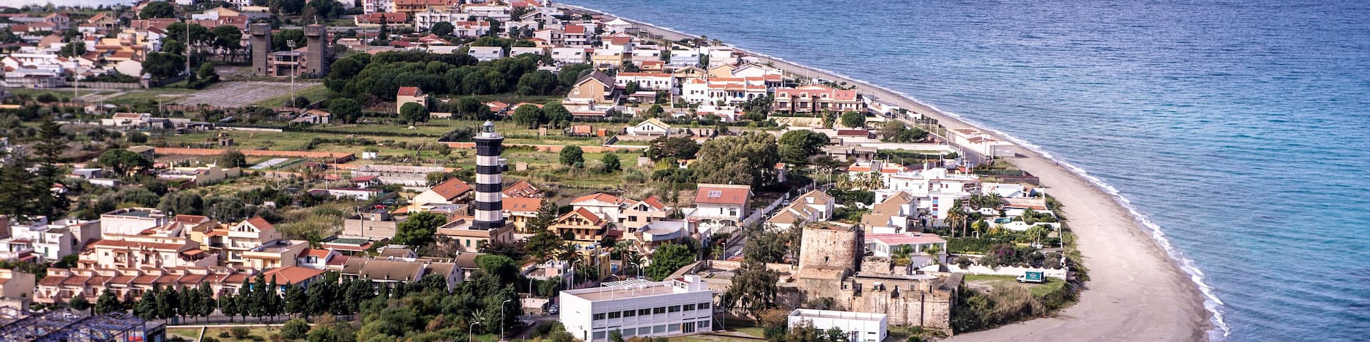 An aerial view of a coastal town with a beach, buildings, and a tower.