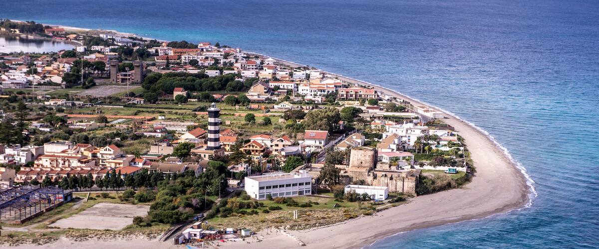 An aerial view of a coastal town with a beach, buildings, and a tower.