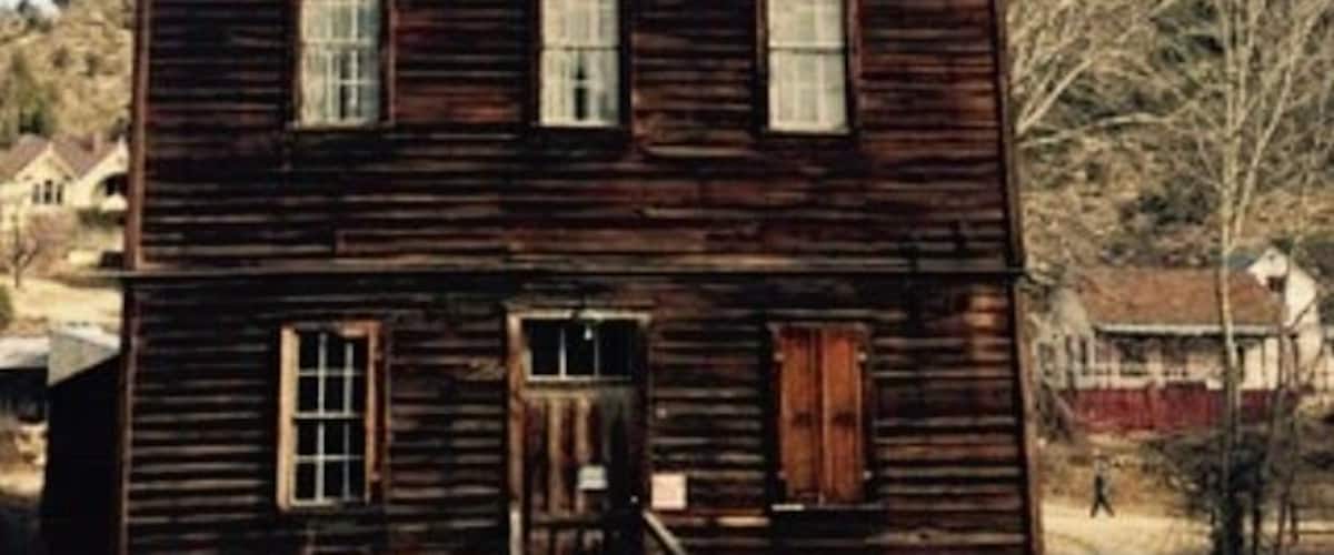 A rustic wooden house with a porch and a small staircase leading to the front door.