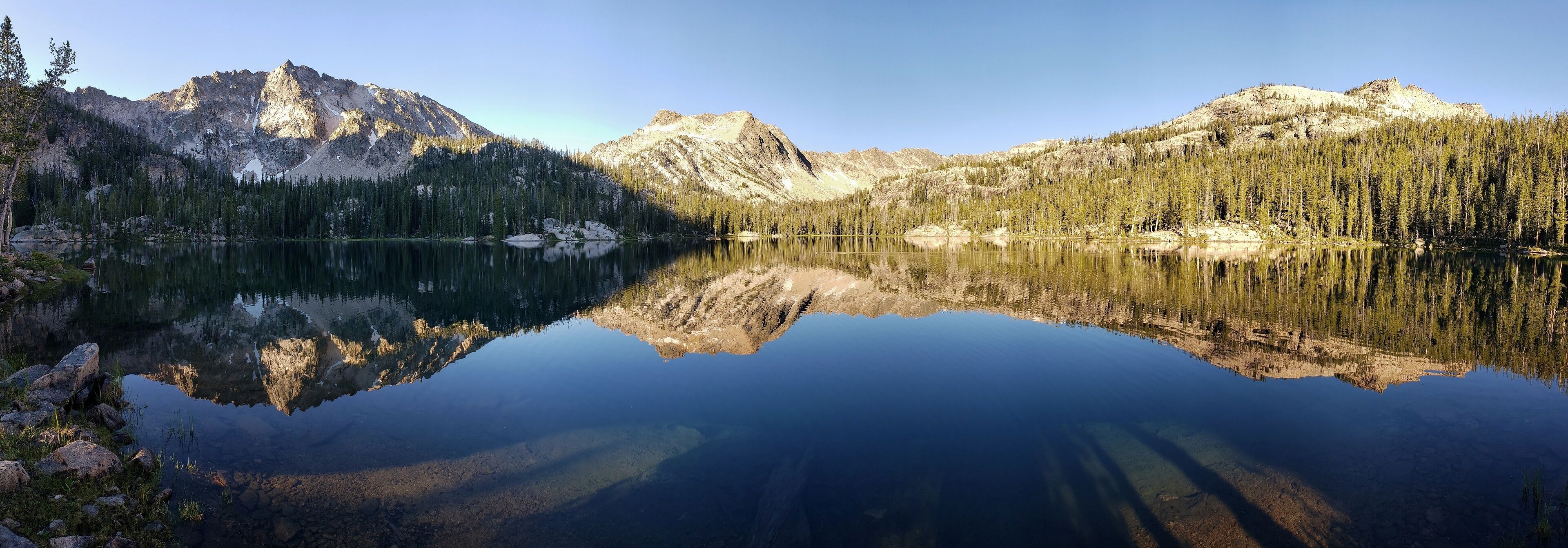 A mountain lake with clear reflections of the surrounding peaks and dense forest.