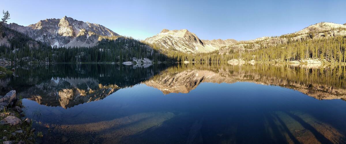 A mountain lake with clear reflections of the surrounding peaks and dense forest.