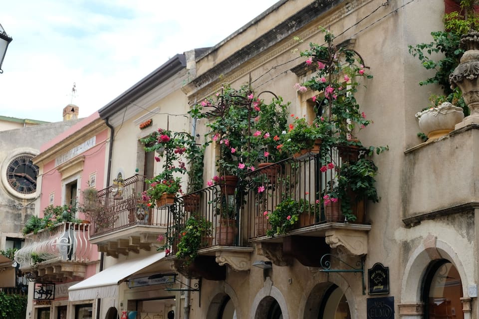 A historic building with ornate balconies, pink flowers, and a street lamp.